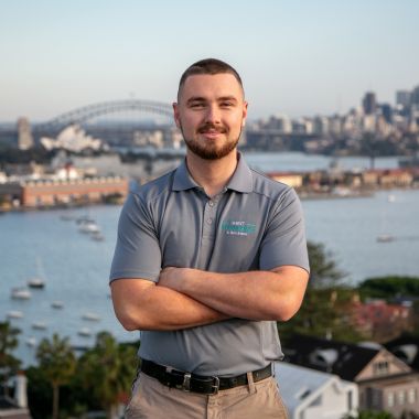 Max, skilled tradesman at Mint Plumbing, with the ocean stretching behind him.