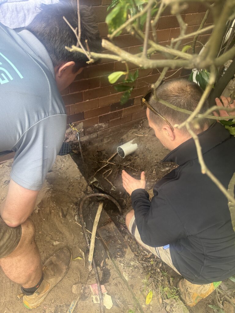 Two plumbers carrying out pipe relining work in Randwick, with tools and equipment laid out beside an open access point.