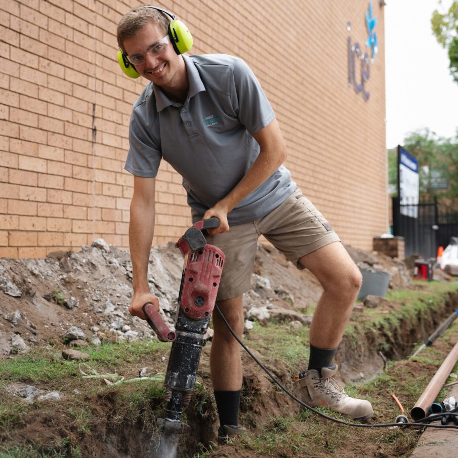 Mint Plumbing & Relining professional working on outdoor drainage repairs.